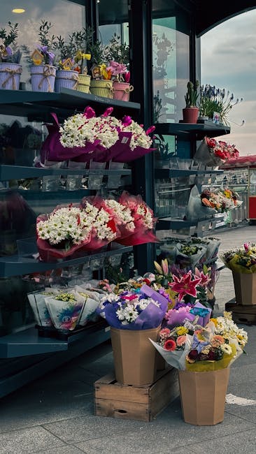 A display of fresh floral arrangements and bouquets at a flower shop, with shelves holding potted plants, small wrapped flowers, and mixed bouquets in pastel-colored wrapping paper and ribbon. The arr